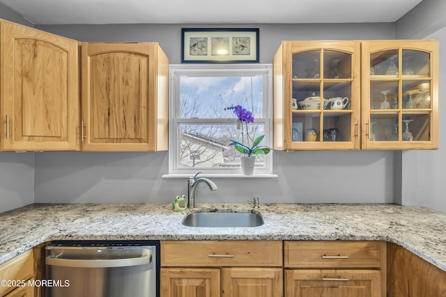 kitchen featuring light stone counters, a sink, glass insert cabinets, and stainless steel dishwasher