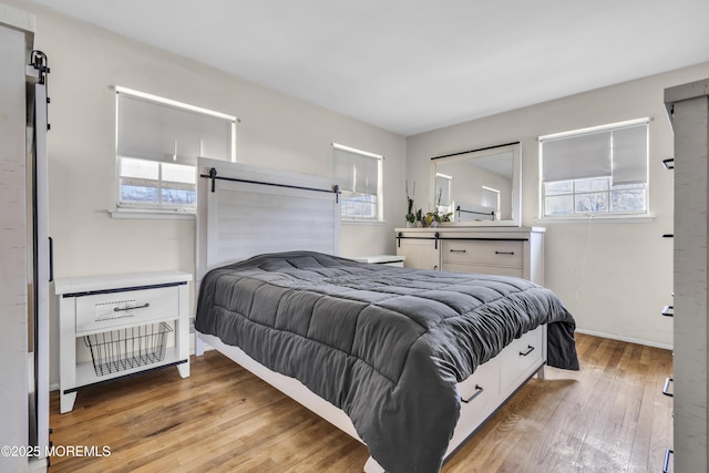 bedroom featuring a barn door, baseboards, and light wood-style flooring