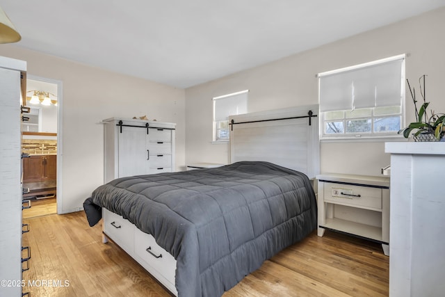 bedroom featuring ensuite bath, light wood-style floors, and a barn door