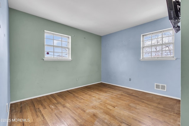 empty room with baseboards, visible vents, wood-type flooring, and a healthy amount of sunlight