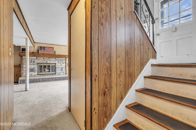 staircase featuring a stone fireplace, wood walls, and carpet floors