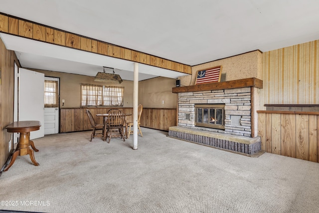 carpeted living room featuring a stone fireplace, wainscoting, and wood walls