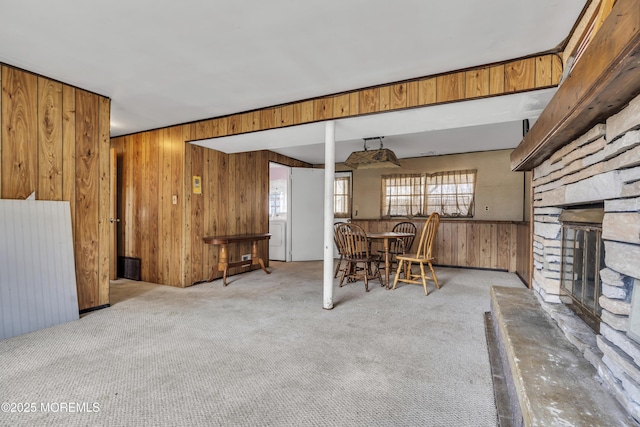 unfurnished living room with a stone fireplace, wooden walls, and carpet floors