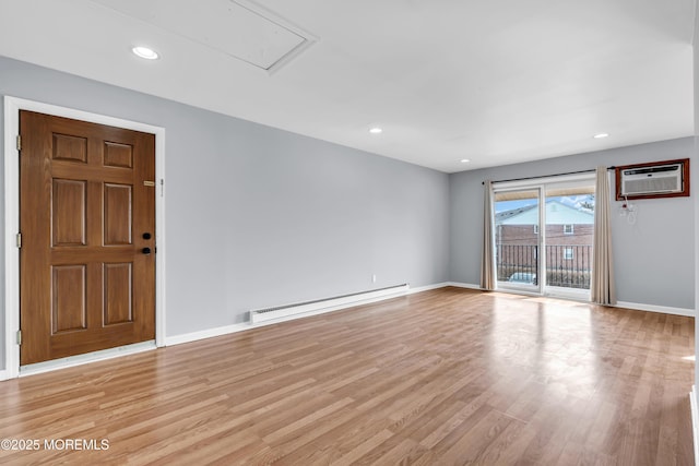 spare room featuring baseboards, an AC wall unit, light wood-type flooring, attic access, and baseboard heating