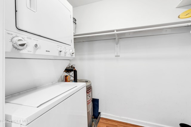 clothes washing area with laundry area, baseboards, stacked washer / drying machine, and light wood-style floors