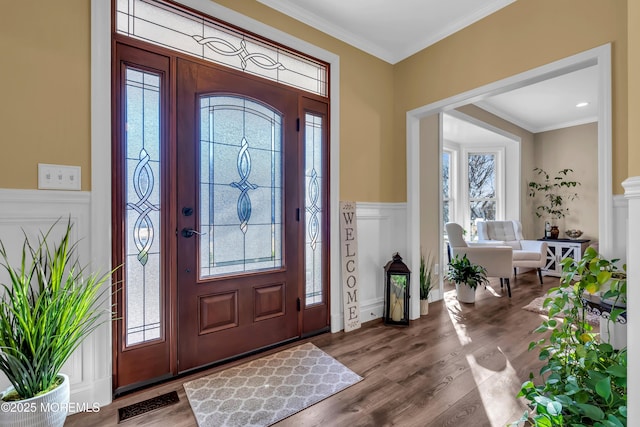 foyer with crown molding, a decorative wall, wood finished floors, and a wainscoted wall