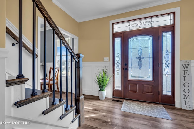 entryway featuring stairway, wood finished floors, visible vents, wainscoting, and a decorative wall