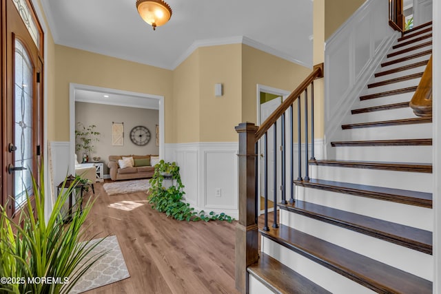 foyer featuring crown molding, light wood-style flooring, and wainscoting