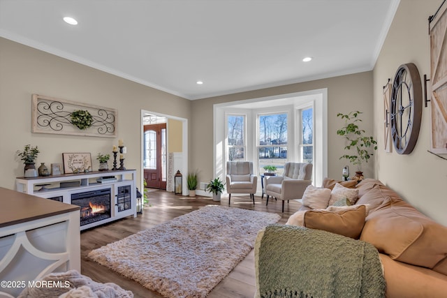 living room featuring a glass covered fireplace, recessed lighting, wood finished floors, and ornamental molding