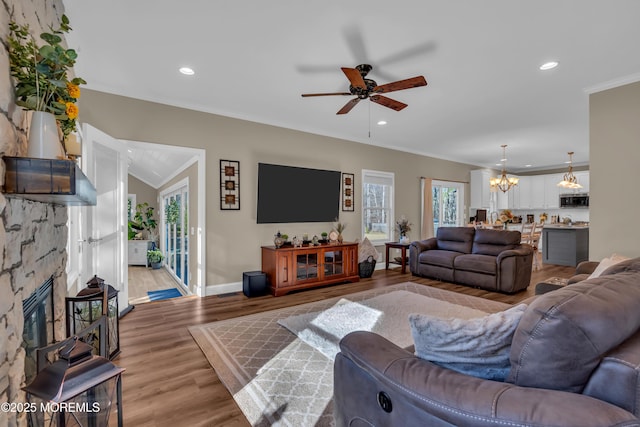 living room with light wood-style flooring, ornamental molding, recessed lighting, a stone fireplace, and baseboards