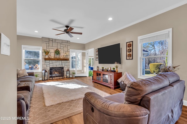 living room featuring a ceiling fan, light wood finished floors, recessed lighting, ornamental molding, and a stone fireplace