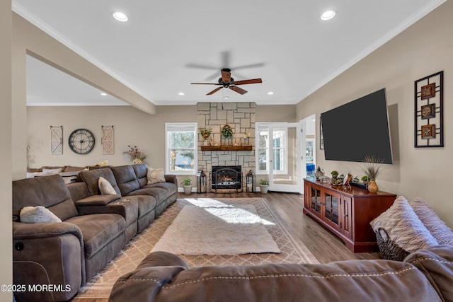 living area featuring a ceiling fan, wood finished floors, recessed lighting, a stone fireplace, and crown molding