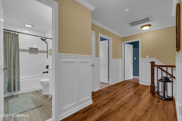 hallway with wood finished floors, visible vents, ornamental molding, stairs, and wainscoting