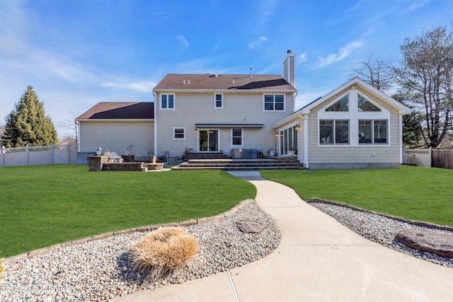 rear view of house with entry steps, a lawn, a chimney, and fence