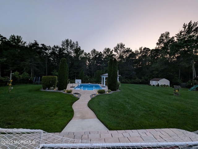 yard at dusk featuring an outdoor pool and an outdoor structure