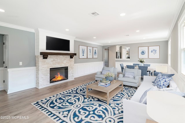 living area with a wainscoted wall, crown molding, wood finished floors, and visible vents