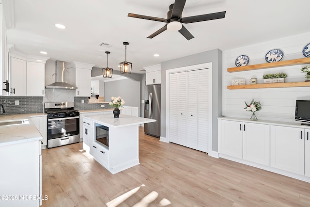 kitchen featuring a sink, wall chimney range hood, white cabinetry, appliances with stainless steel finishes, and light wood finished floors