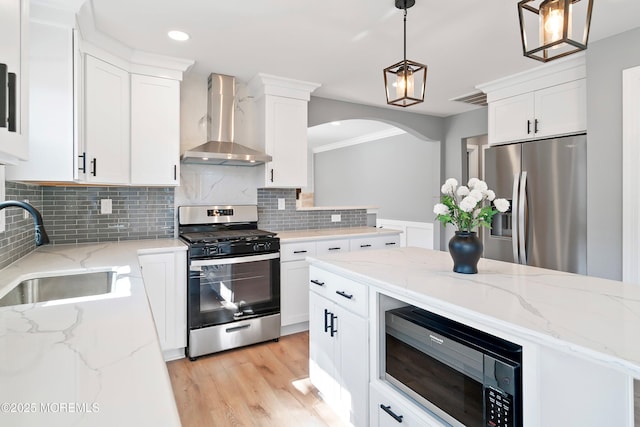 kitchen featuring wall chimney range hood, decorative backsplash, white cabinets, stainless steel appliances, and a sink