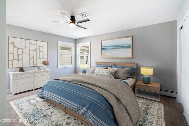 bedroom featuring visible vents, baseboard heating, a ceiling fan, and wood finished floors