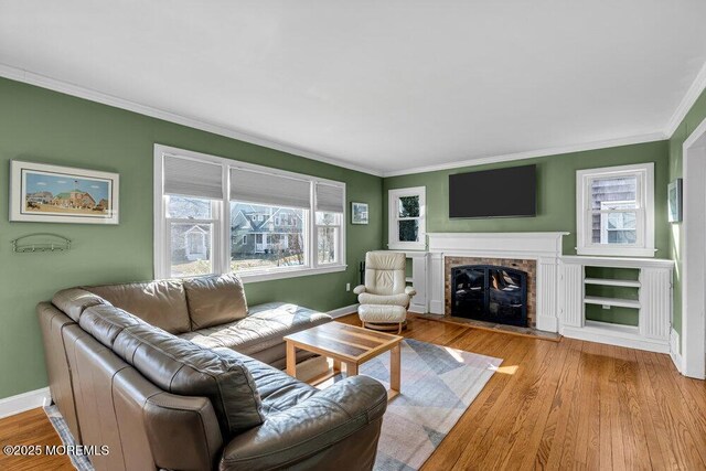 living area featuring a fireplace with flush hearth, wood finished floors, baseboards, and ornamental molding