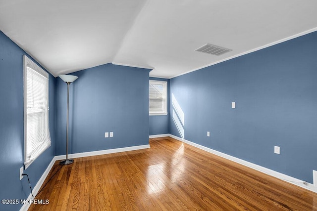 empty room with visible vents, crown molding, baseboards, vaulted ceiling, and wood finished floors