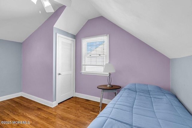 bedroom featuring a closet, baseboards, wood finished floors, and vaulted ceiling