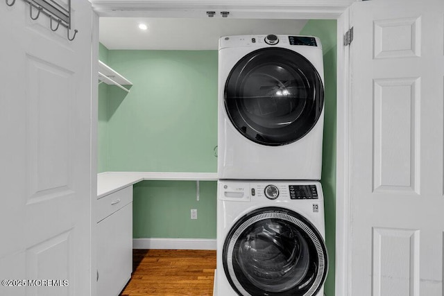 washroom with laundry area, stacked washer and dryer, wood finished floors, and baseboards