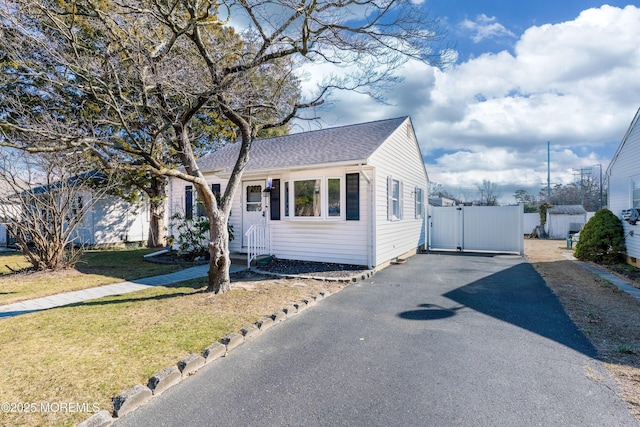 view of front of house featuring a front yard, a gate, driveway, and a shingled roof