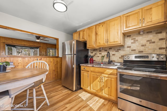 kitchen featuring light wood finished floors, wooden walls, backsplash, stainless steel appliances, and a sink