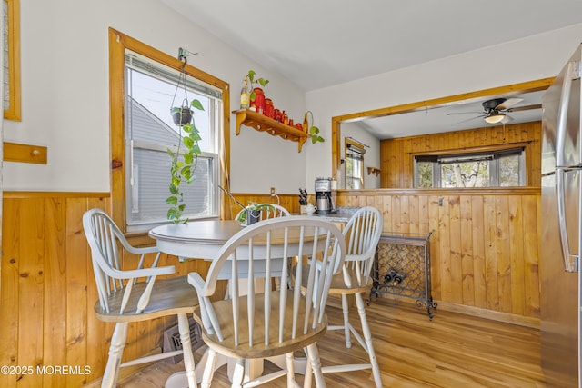 dining room featuring a wainscoted wall, wood walls, ceiling fan, and wood finished floors