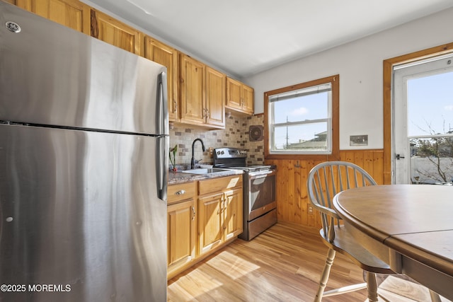 kitchen with wooden walls, a wainscoted wall, light wood-style flooring, appliances with stainless steel finishes, and a sink