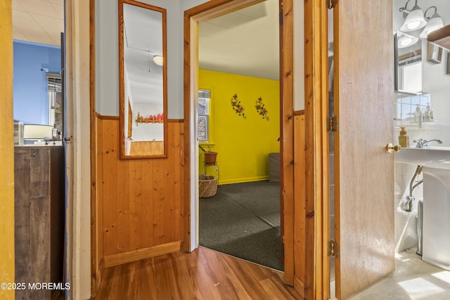 hallway featuring baseboards, wooden walls, and wood finished floors