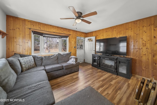 living room featuring wooden walls, baseboards, a ceiling fan, and wood finished floors