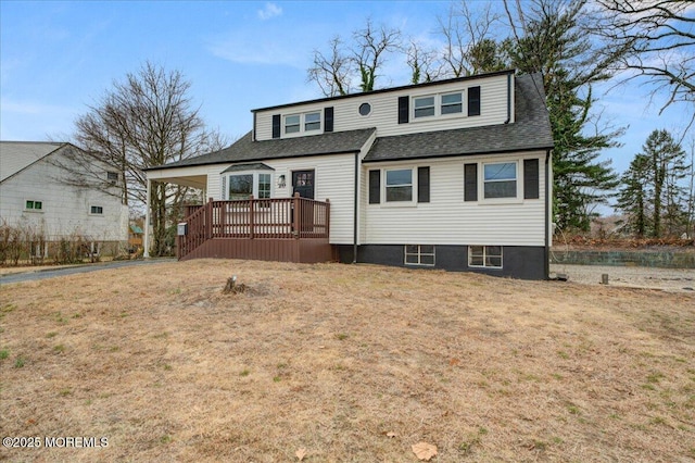 view of front of home with a front lawn, a wooden deck, roof with shingles, a carport, and driveway