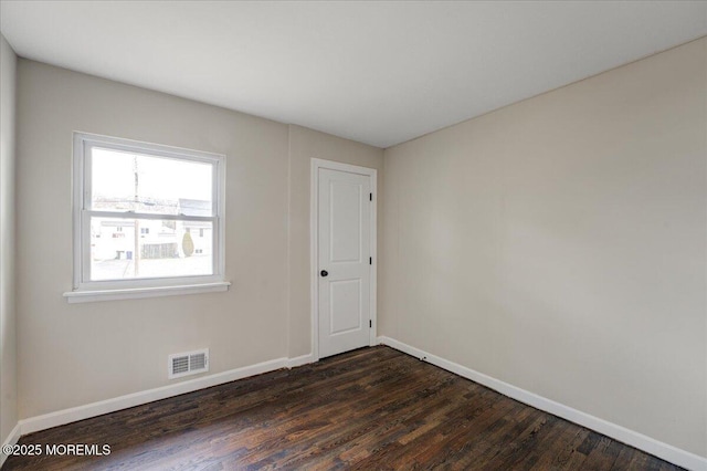 empty room featuring dark wood-style floors, visible vents, and baseboards