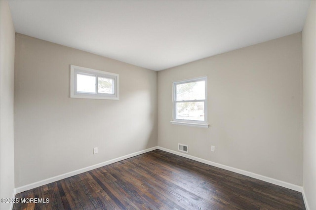 spare room featuring dark wood finished floors, visible vents, and baseboards