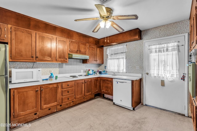 kitchen with white appliances, brown cabinetry, light countertops, and under cabinet range hood