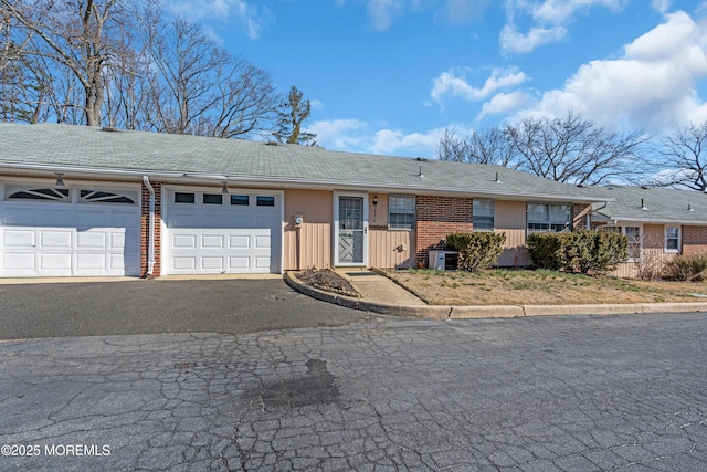 view of front of house featuring aphalt driveway, an attached garage, cooling unit, and brick siding