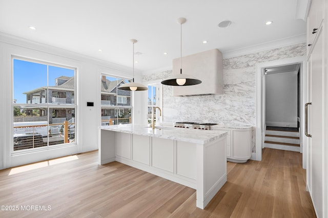 kitchen featuring light wood finished floors, ornamental molding, a kitchen island with sink, and a sink