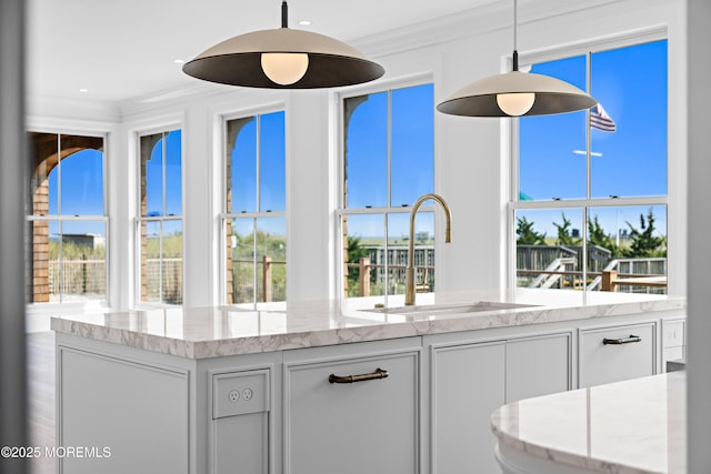 kitchen with pendant lighting, ornamental molding, a sink, white cabinets, and light stone countertops