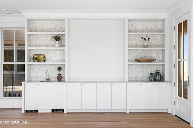 bar with a sink, light wood-type flooring, built in features, and ornamental molding