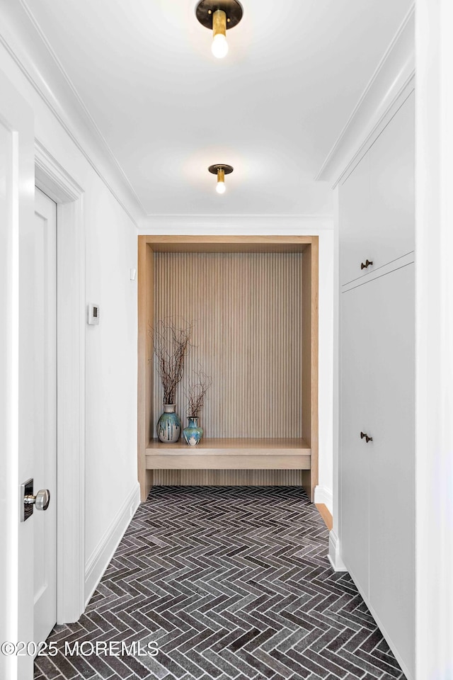 corridor featuring brick floor, baseboards, and crown molding