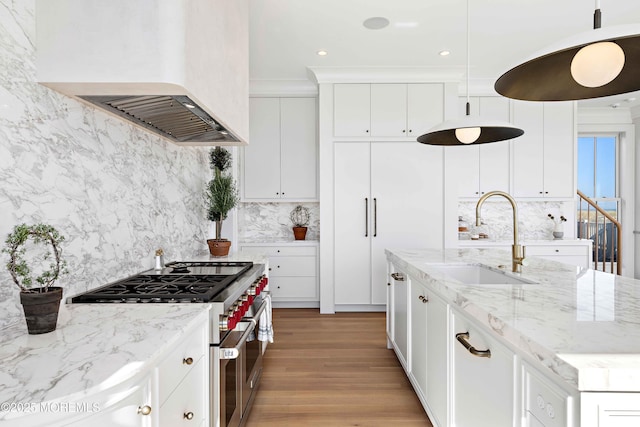 kitchen with a sink, double oven range, white cabinetry, and premium range hood