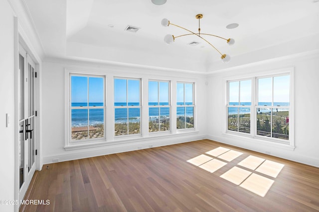 unfurnished sunroom with a raised ceiling, a notable chandelier, visible vents, and a water view