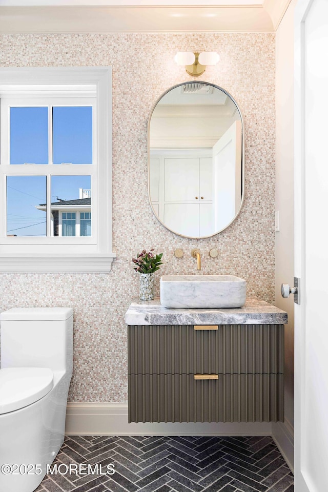 half bath with brick floor, baseboards, toilet, and vanity