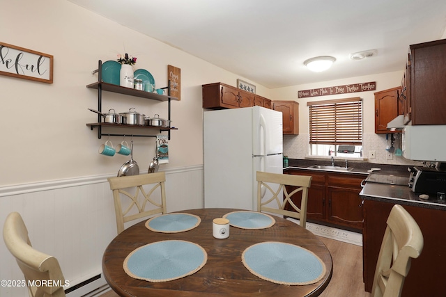 kitchen featuring a wainscoted wall, a sink, under cabinet range hood, dark countertops, and freestanding refrigerator