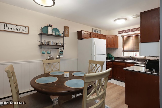 kitchen with a sink, dark countertops, freestanding refrigerator, light wood-style floors, and wainscoting