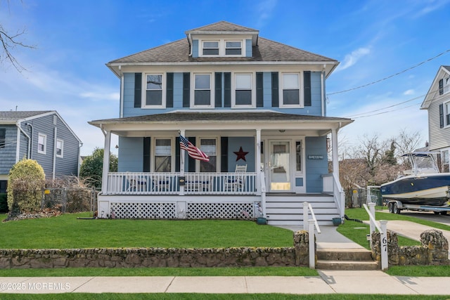 american foursquare style home with roof with shingles, covered porch, and a front yard