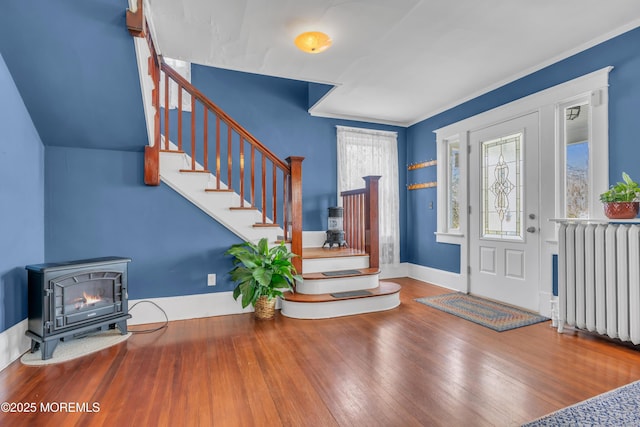 foyer featuring baseboards, stairs, radiator heating unit, a wood stove, and hardwood / wood-style flooring