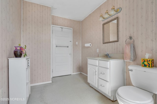 bathroom featuring vanity, toilet, baseboards, and wallpapered walls